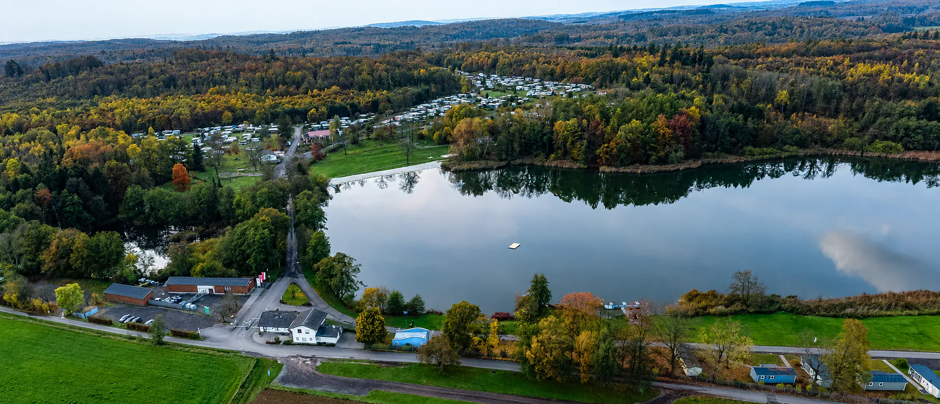 Luftaufnahme des Gederner Sees mit Campingpark, Badestrand und herbstlich gefärbtem Wald – ideal für einen Tagesausflug in Hessen
