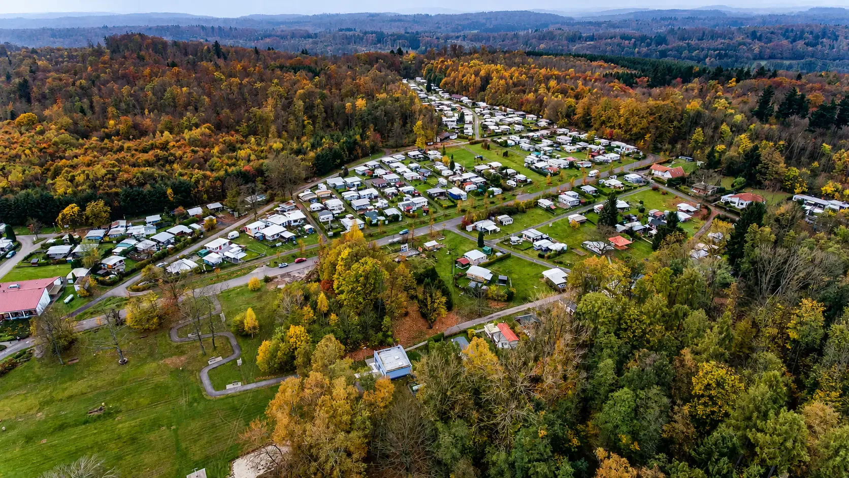 Luftaufnahme des Campingparks am Gederner See im Herbst mit Campingwiesen, Unterkünften und umliegendem Wald