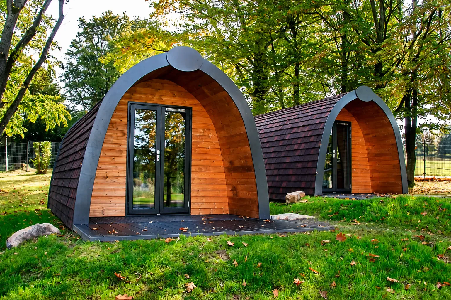 Zwei Woodlodges zwischen Bäumen auf der Wiese
