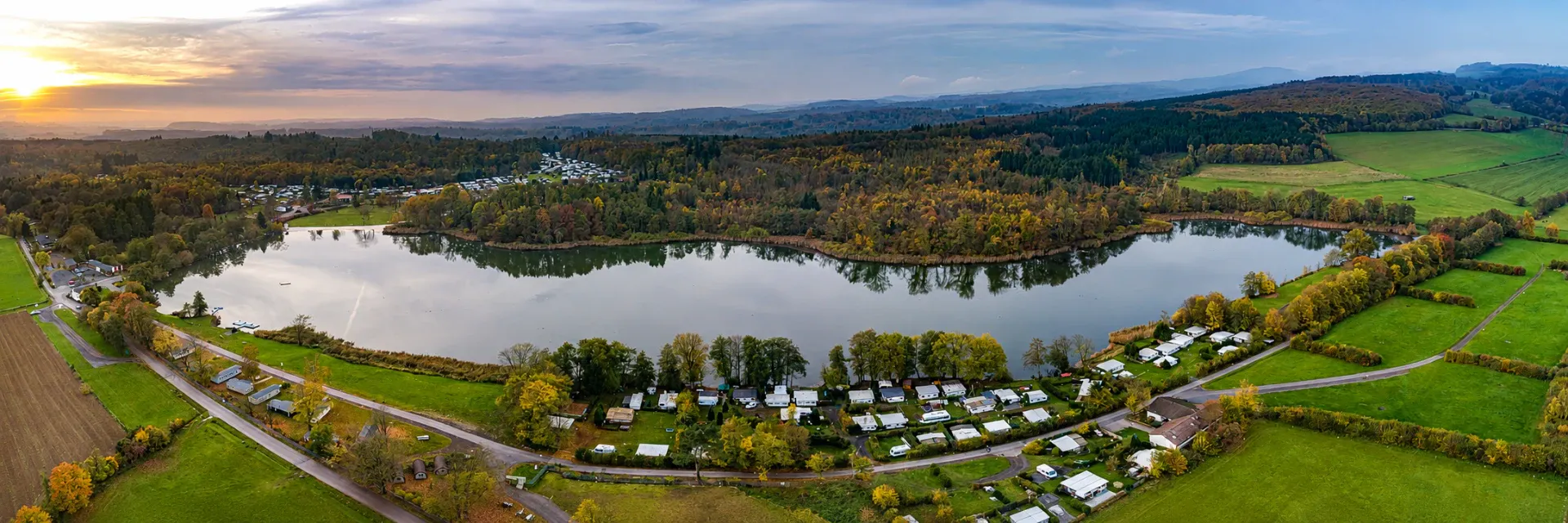Luftaufnahme des Campingparks am Gederner See im Herbst mit Wald und Bergen im Hintergrund