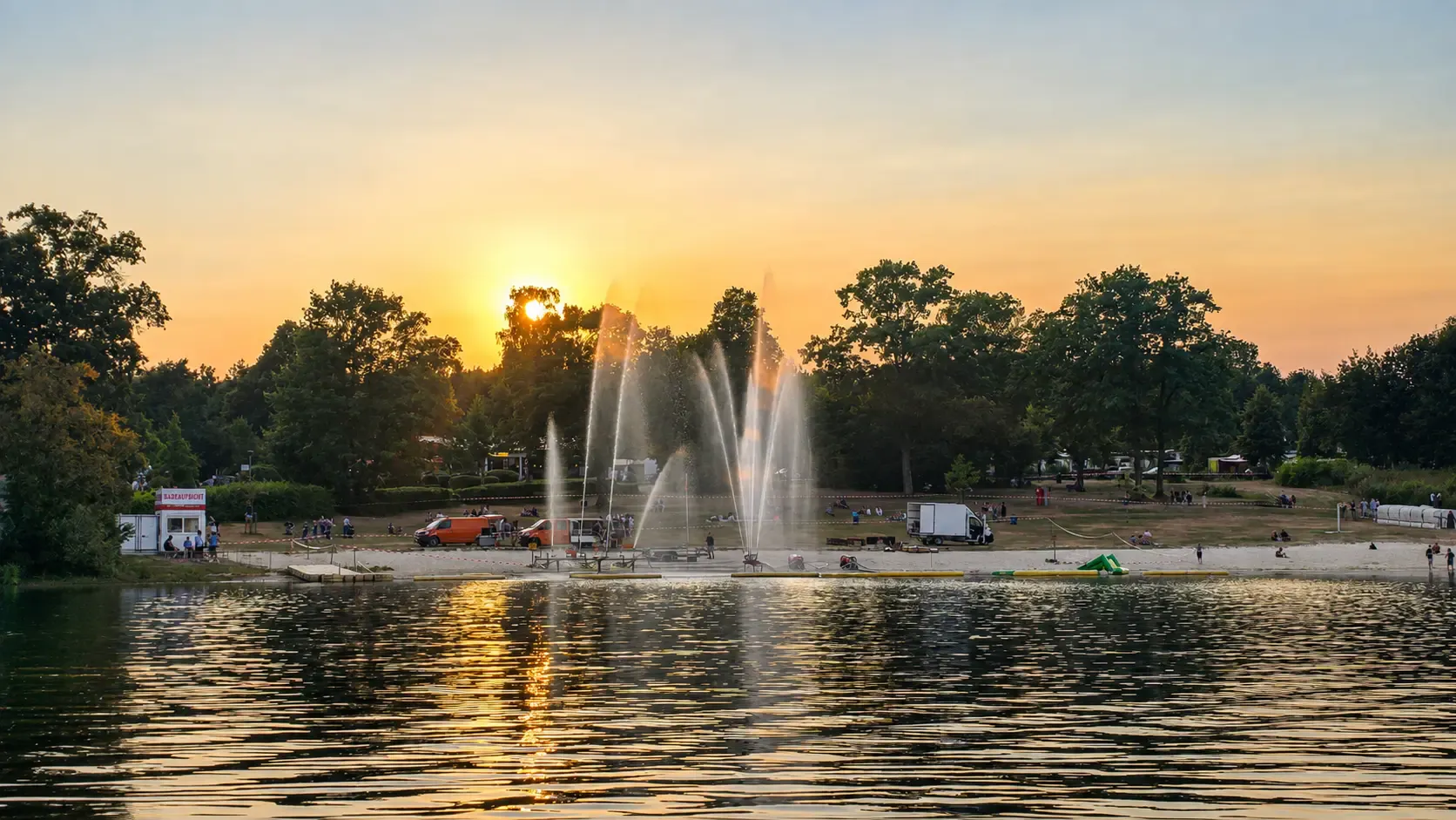 Sonnenuntergang über dem Gederner See mit beleuchteten Springbrunnen während einer Veranstaltung